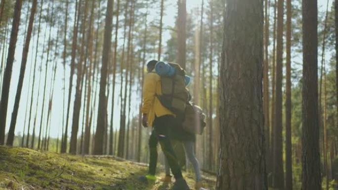 一对年轻的黑人男女在前往树林的过程中，带着慢动作的背包在树林中行走。旅游期间，两名非洲人背着背包穿过