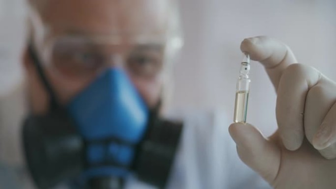 科学家在蓝色呼吸器和防护眼镜中的极端特写镜头，冠状病毒疫苗的开发者拿着白色透明安瓿。医生看了新疫苗。