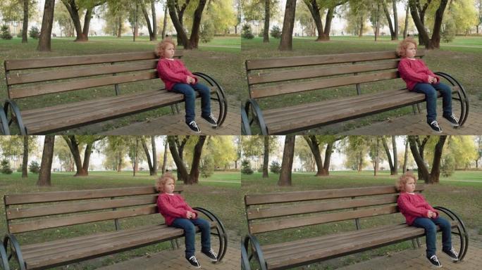 孤独的红发孩子坐在公园的长凳上，被遗弃的孩子感到沮丧