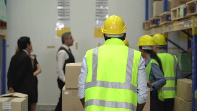 一名男性工人戴着安全帽和反光背心在仓库里推动托盘千斤顶