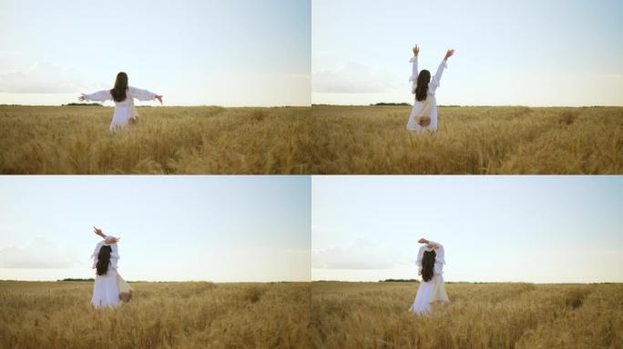 快乐的黑发女人在夏日走在黑麦田里，举起手来欣赏大自然的美丽