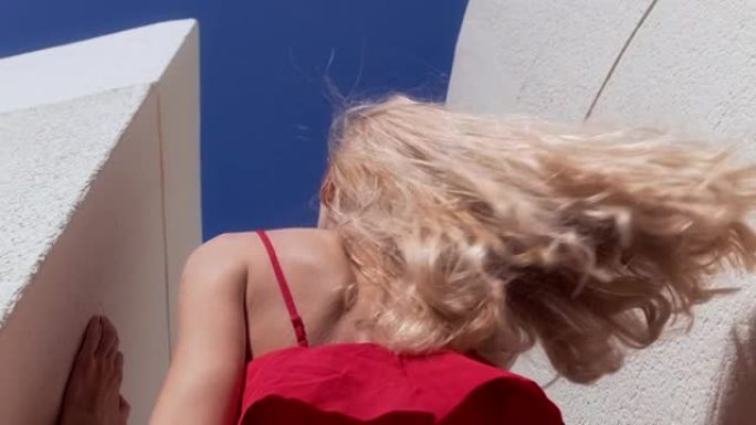 阳光充足的楼梯上诱人的女人。穿着红色漂亮的连衣裙。用相机调情