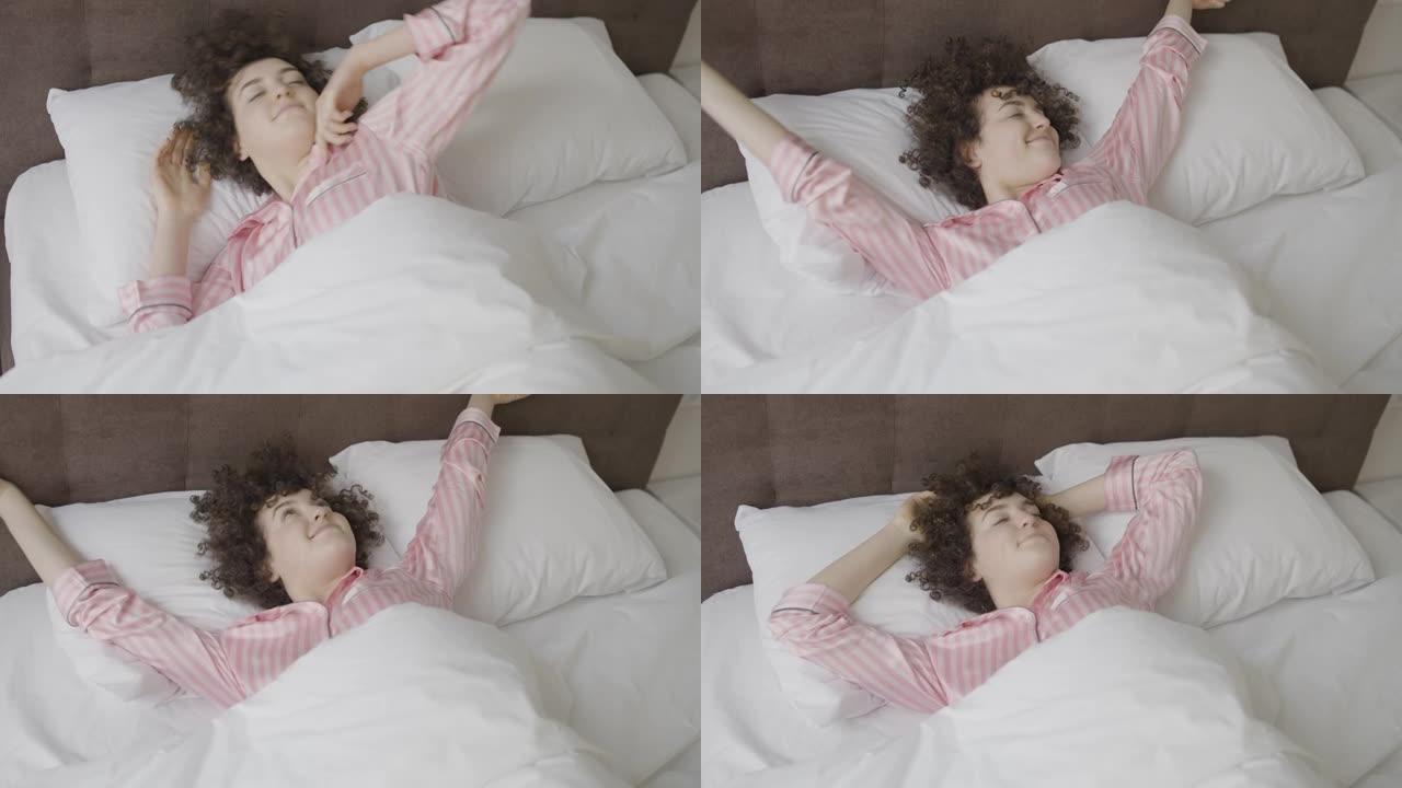 女人在舒适的床上愉快地醒来，睡得安稳，享受生活