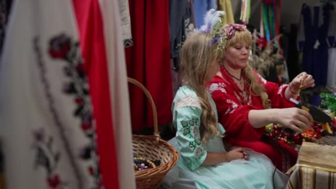 侧视图熟练的乌克兰妇女与古玩女孩在工艺品店里制作传统的花环。才华横溢的母亲在室内慢动作教女儿。生活方