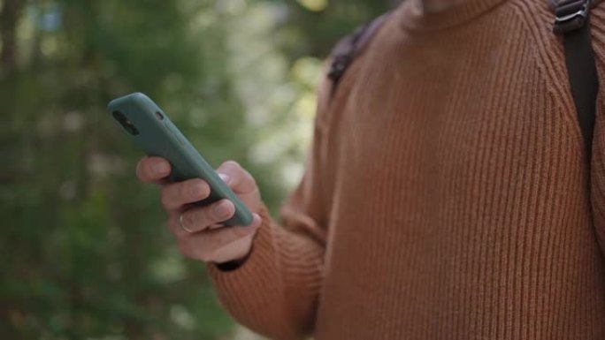 在森林中穿行的男性旅行者手中的手机特写。社交网络导航器和信使。用手机在树林里散步