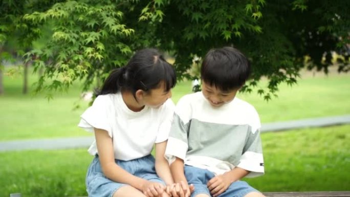 微笑的小学男孩和女孩坐在公园的长凳上