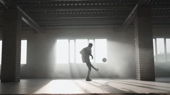 一个黑人在阳光下的地下停车场用球做足球自由泳。慢动作射击在地下停车场玩弄球。