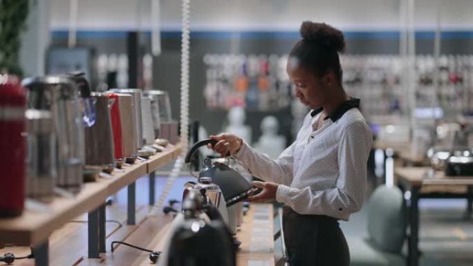 黑人妇女正在检查家用电器商店的电热水壶模型，美国黑人女士正在陈列柜上观看展览样本