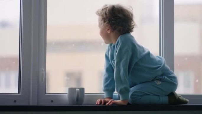 快乐无忧无虑的童年，冬天白天，穿着蓝色睡衣的小男孩坐在公寓的窗台上