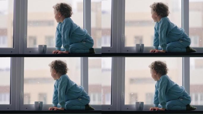 快乐无忧无虑的童年，冬天白天，穿着蓝色睡衣的小男孩坐在公寓的窗台上