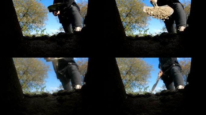一个身穿深色衣服、面无人色的人正对着乌云密布的蓝天挖一个方形的坑。从坟墓的角度看，铲土洒入坟墓。慢镜