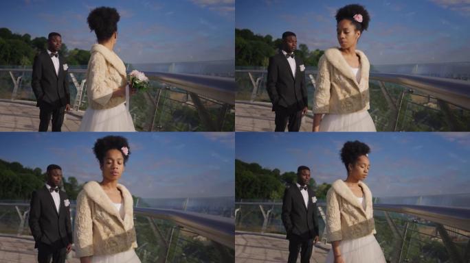 悲伤的非洲裔美国新娘穿着漂亮的婚纱，回头看新郎，转向镜头。不幸的女人在桥上户外结婚的肖像。悲伤和婚姻