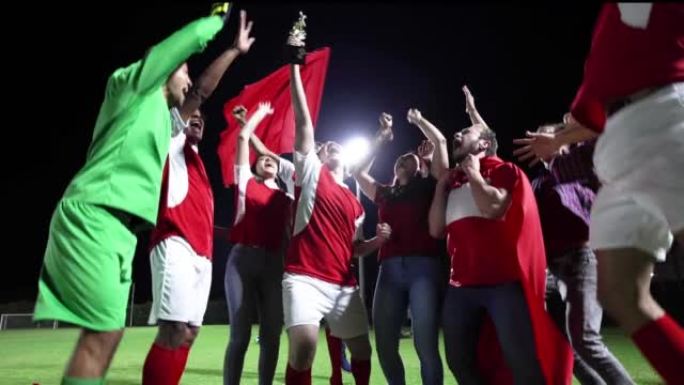激动的一群球迷和足球运动员庆祝他们的球队的胜利并举起奖杯