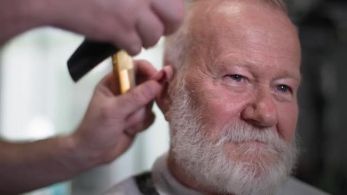 有吸引力的老年男子与灰色胡子做头发修剪在一个现代理发师沙龙，特写