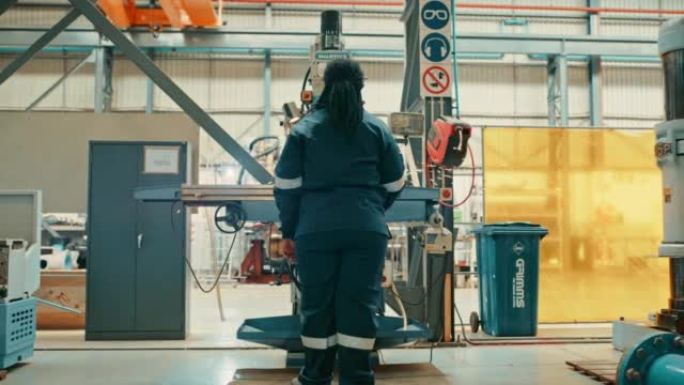 非洲女工程师使用在仓库中工作的电机切割金属。为钢铁厂工作的独立年轻女性制造商。女士在车间里操作大型工