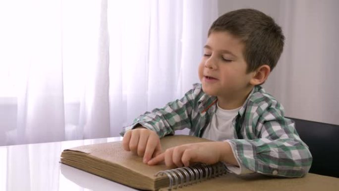 为盲人，生病的小男孩学习，阅读带有字符字体的盲文书，供视障人士坐在餐桌旁