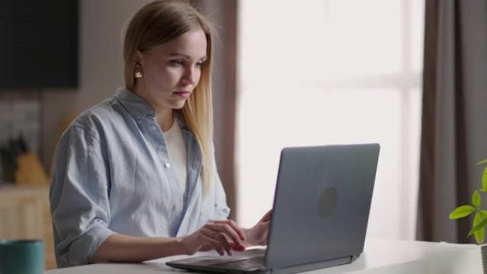 在家中的移动办公室。年轻女子坐在家里的厨房里使用笔记本电脑工作。在室内学习或工作的生活方式女孩。自由