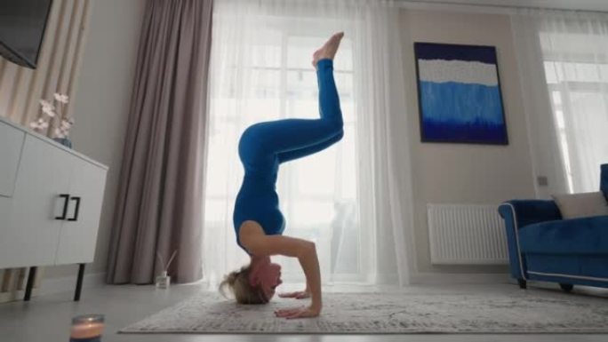 一个运动的美女在家里用头和手表演站立。在他自己公寓的地毯上。平衡练习