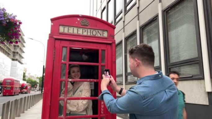 可爱的高加索夫妇在英国伦敦旅游时在一个标志性的旅游红色电话亭一起拍照