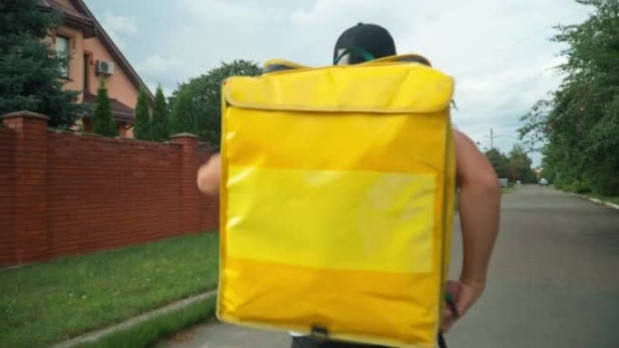 当年轻人穿着背包走路时，实时摄像机跟随黄色的送货袋。高加索信使带着背包在镇上的郊区路上漫步。交付服务