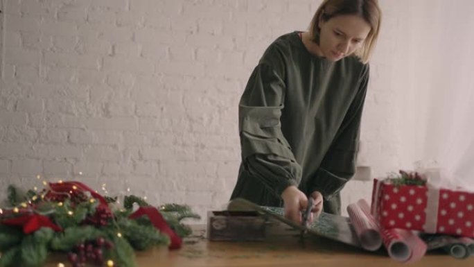 肖像一名年轻女子用花环在木桌上装饰礼物，翻过来放在桌子上，一个用丝带压碎的现成的圣诞盒