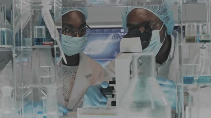 从事显微镜工作的非洲族裔科学家。浏览实验室玻璃器皿