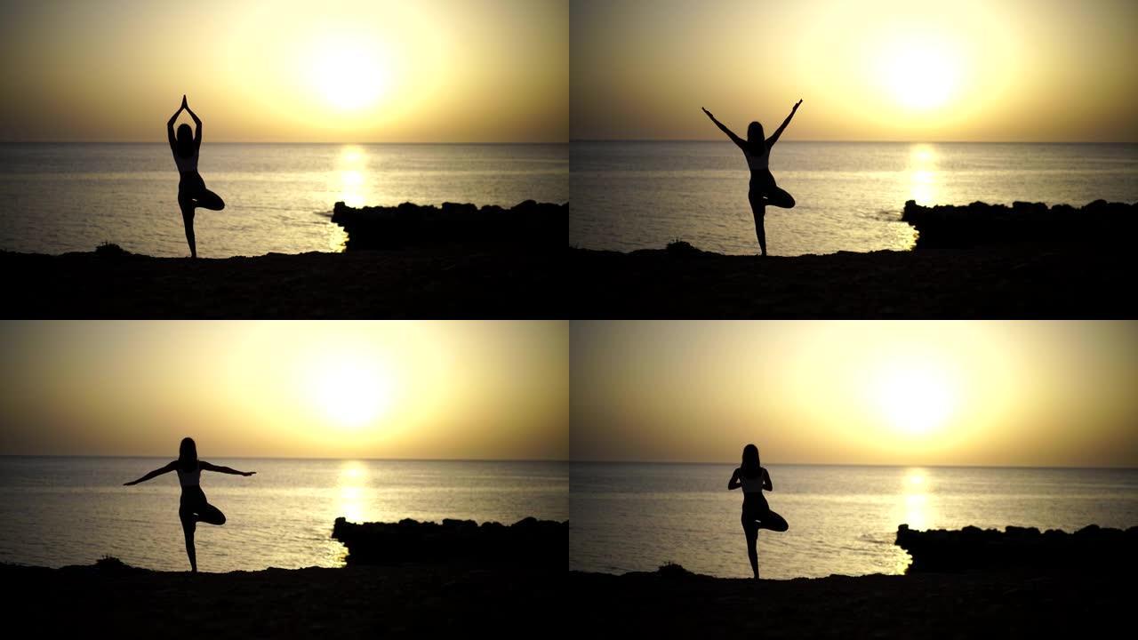 日落映衬的海滩附近练习瑜伽的年轻女子