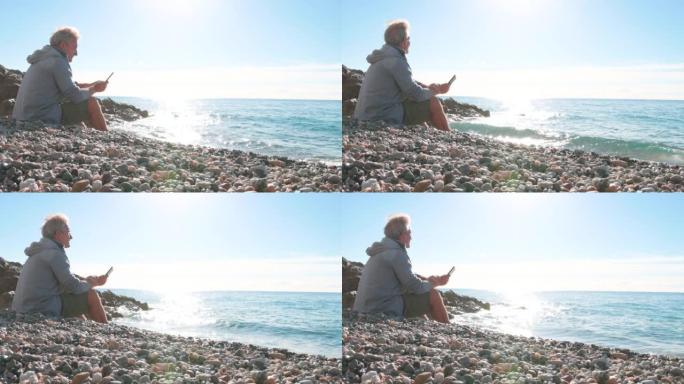成熟的男人在圆石滩上使用电子阅读器