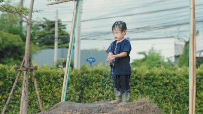 亚洲男孩在户外玩泥浆滑梯后洗泥
