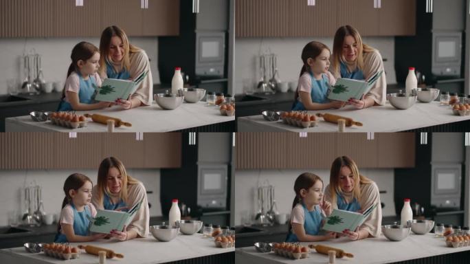 快乐的母亲和小女孩正在阅读食谱中的面团收据，妈妈和女儿正在家庭厨房做饭
