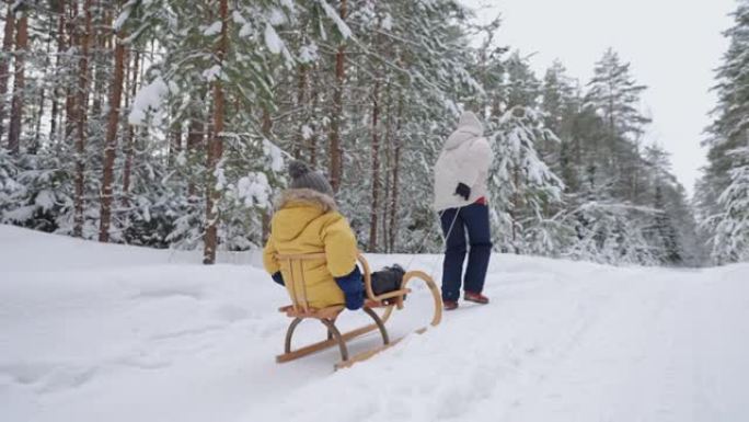 冬天在大自然中休息，母亲和小男孩在白雪皑皑的林地里骑着雪橇