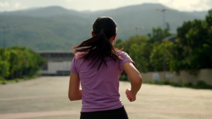 亚洲女子在运动场跑步，背景是一座体育场和一座傍晚的大山。