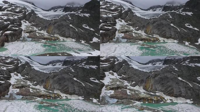 从上面看雄伟的阿尔卑斯山。陡峭的山坡被雪覆盖，瀑布从湖上掉下来