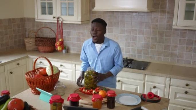 实时摄像机放大到积极的非洲裔美国人在家里的厨房里闻到黄瓜罐头开瓶器的味道。满意的英俊年轻人在室内准备