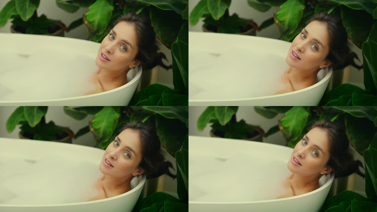 年轻女子在浴室内郁郁葱葱的绿色花园里洗泡泡浴。对着镜头微笑