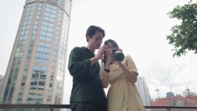 年轻的亚洲女友和男朋友在周末假期在市区内拍照后看着全画幅相机屏幕拍照，旅行情侣场景分享美好的回忆