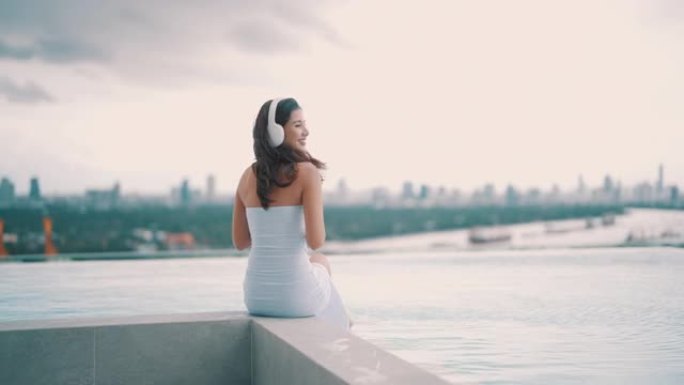 后视图: 亚洲女性戴着耳机听音乐，在池畔愉快地放松