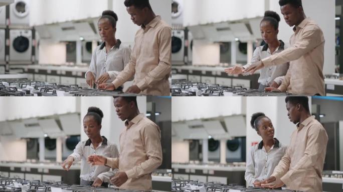 年轻的配偶在商场的家电商店里选择燃气灶，黑人男女正在看烹饪表面并讨论