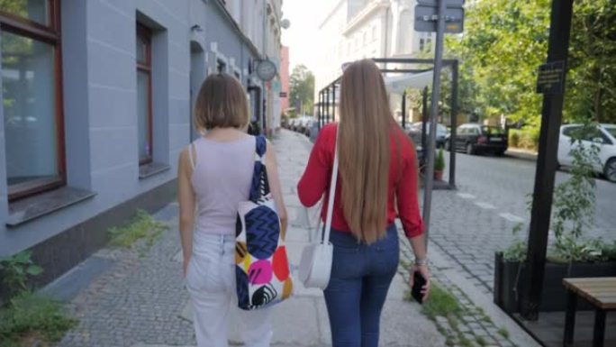 漂亮的年轻女性朋友走在城市的人行道上，互相交流