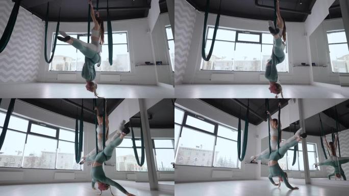 教练和年轻女子在健身房练习悬浮航空体操。在健身俱乐部的绿色吊床上进行空中瑜伽练习的两名年轻美丽的瑜伽
