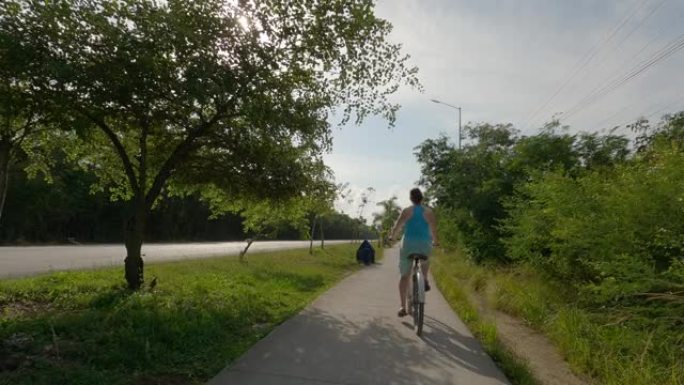 女人沿着丛林小路骑自行车，在马路旁边