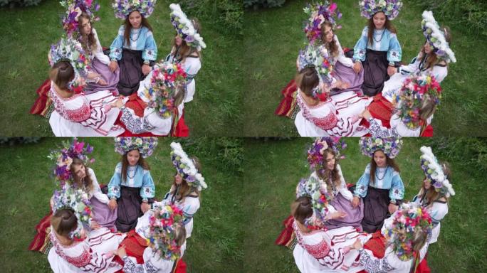 穿着民族服装的乌克兰美女高视角，双手坐在绿色的草地上唱着民歌。正面迷人自信的女士头上的花圈享受民俗。