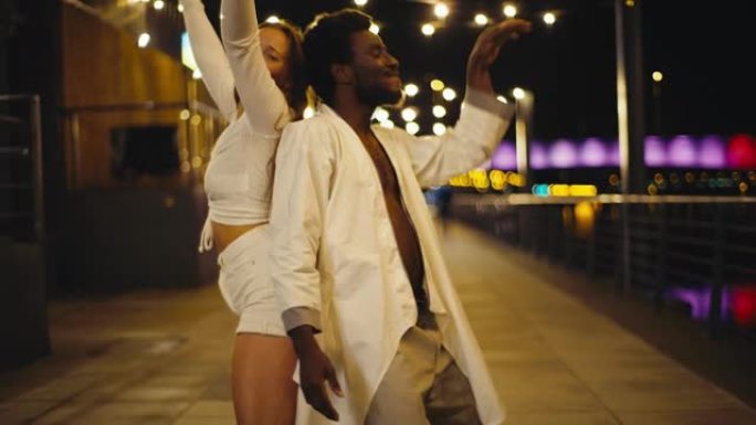 年轻多样的夫妇在潮湿的城市街道上表演现代舞蹈。开心和微笑