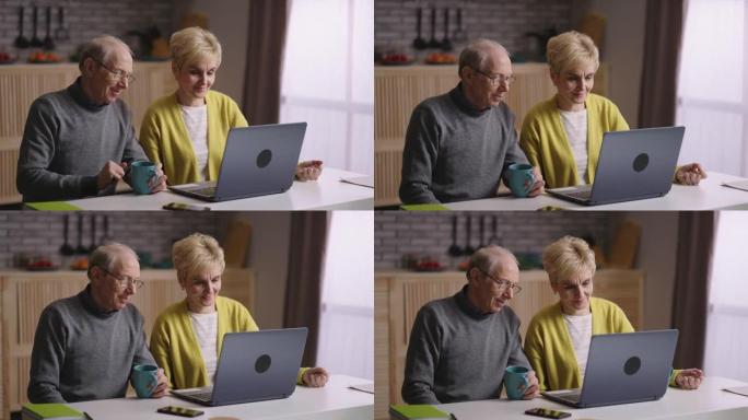 快乐的老配偶正在与朋友或家人通过视频通话聊天，对笔记本电脑的网络摄像头微笑，一起坐在厨房里