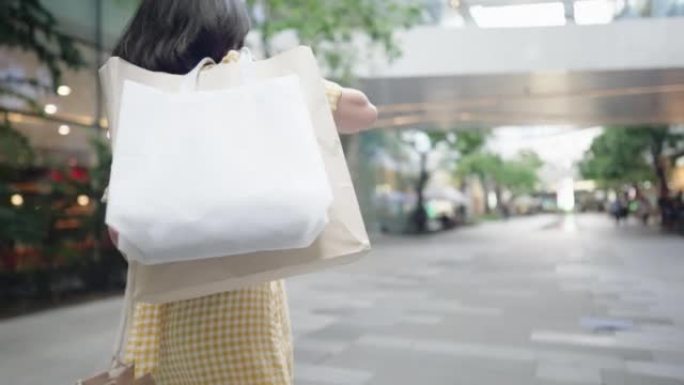 美丽的女人抱着购物袋走路。快乐好身材和心情的顾客带着纸袋走在社区购物中心街上。快乐的黄色礼服女孩离开