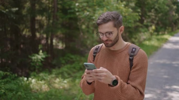一个背着背包的游客沿着森林中的一条土路走，写信息，在互联网上交流，查看内容。特写。