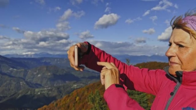 SLO MO高级女徒步旅行者在阳光明媚的山顶上拍照