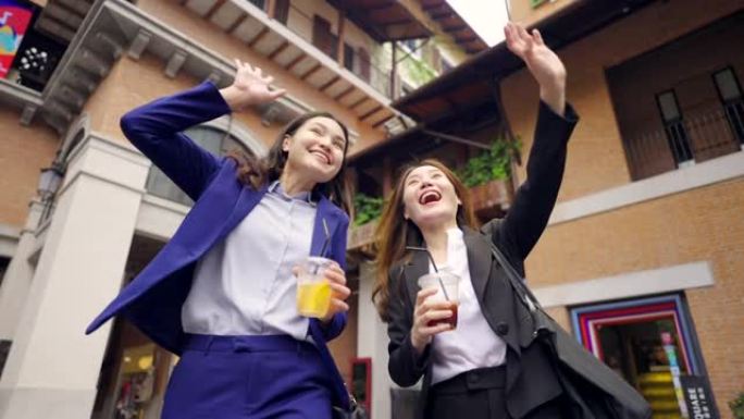 两名亚洲商界女性手持咖啡杯，在咖啡馆外散步，在会议中微笑着玩得开心。