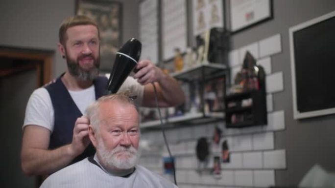 现代发型师为时髦的老年男性客户理发，并在与发型师一起造型时吹干他的头发