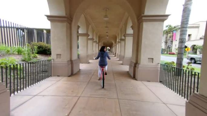 一名女子骑着自行车穿过室外走廊拍摄后